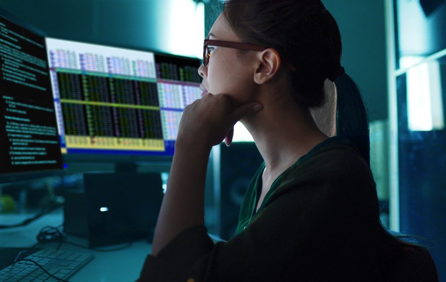 Stock photo of an Asian woman surrounded by computer monitors in a dark room
